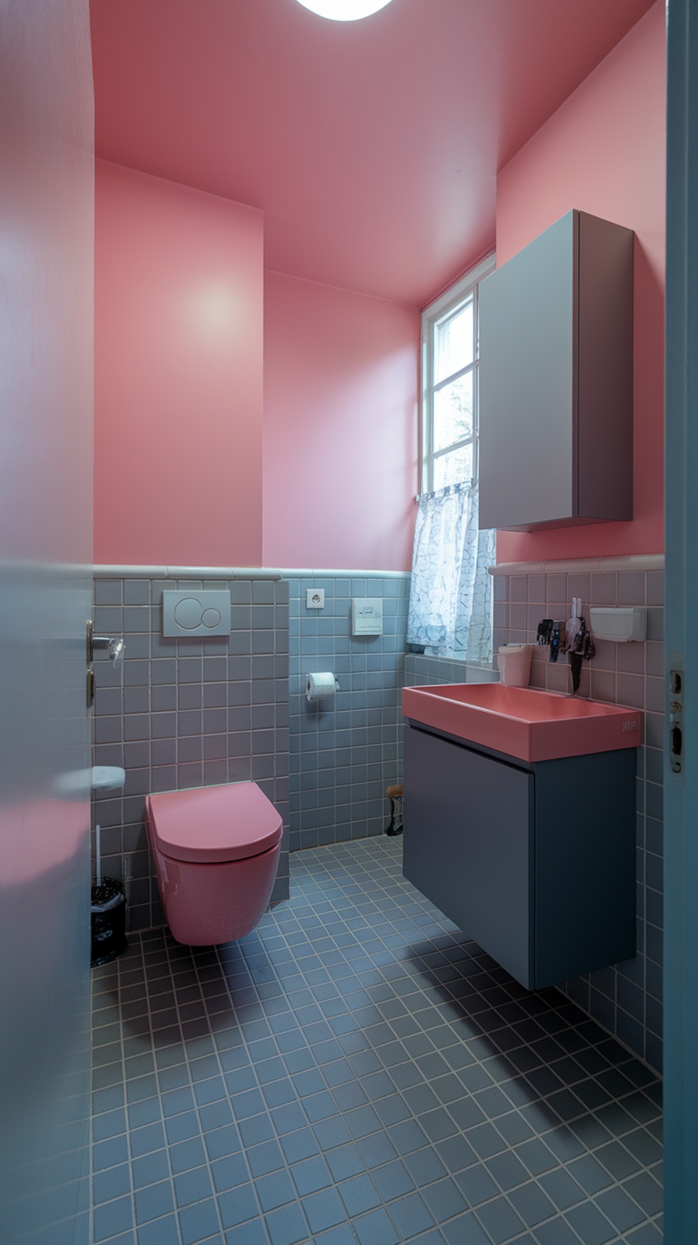 A pink and grey bathroom featuring pink walls, a pink toilet, and grey cabinets.